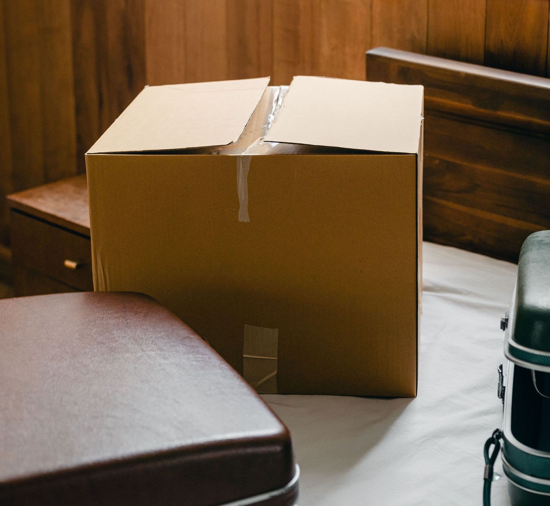 From above of modern suitcases placed near big cardboard box on bed in contemporary apartment